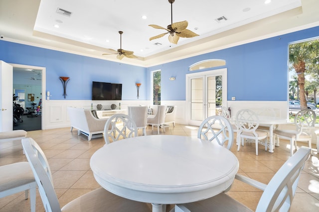 tiled dining space with french doors, a tray ceiling, ceiling fan, and ornamental molding