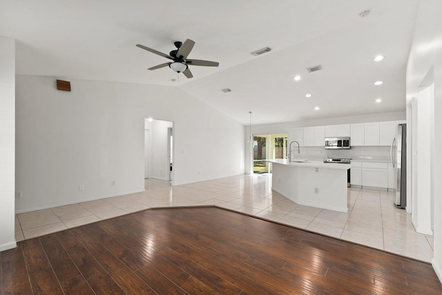 unfurnished living room with ceiling fan, sink, light hardwood / wood-style floors, and vaulted ceiling