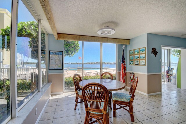 dining space with a textured ceiling, plenty of natural light, a water view, and light tile patterned floors