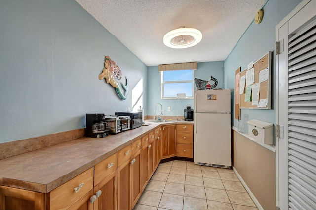 kitchen featuring a textured ceiling, white fridge, light tile patterned floors, and sink