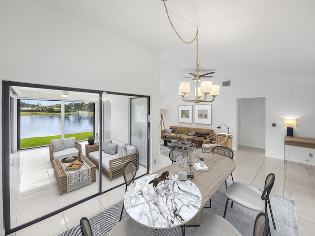 tiled dining area featuring ceiling fan with notable chandelier, a water view, and high vaulted ceiling