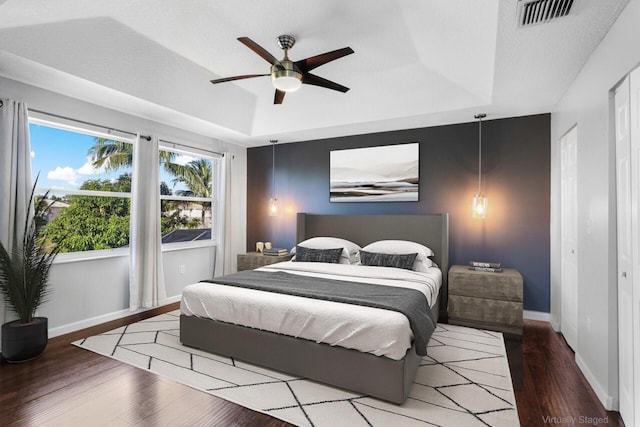 bedroom with hardwood / wood-style floors, ceiling fan, a textured ceiling, and a tray ceiling