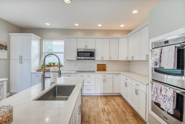 kitchen with backsplash, light wood-type flooring, stainless steel appliances, sink, and white cabinetry