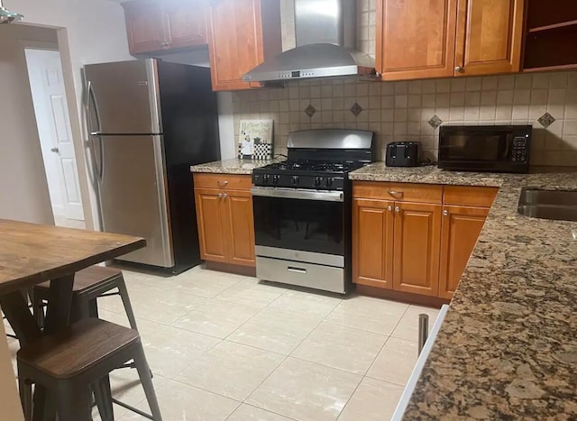 kitchen featuring backsplash, light stone counters, wall chimney exhaust hood, and stainless steel appliances