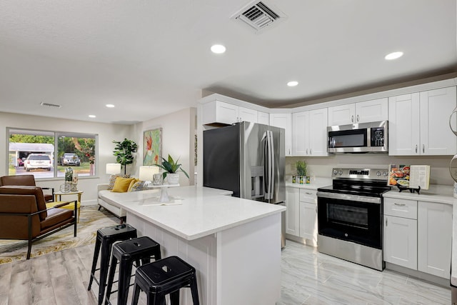 kitchen with a center island, white cabinets, appliances with stainless steel finishes, light stone counters, and a breakfast bar area