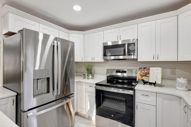 kitchen featuring white cabinets, light wood-type flooring, stainless steel appliances, and light stone counters