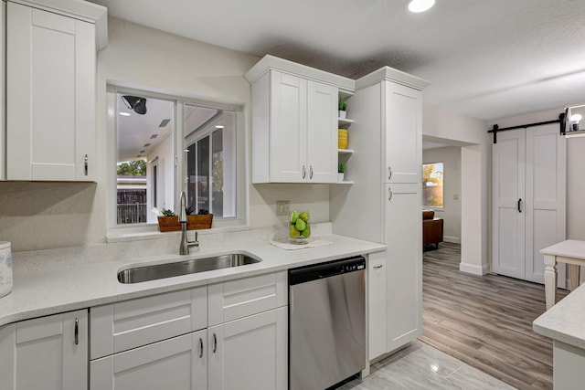 kitchen featuring a barn door, white cabinetry, sink, and stainless steel dishwasher