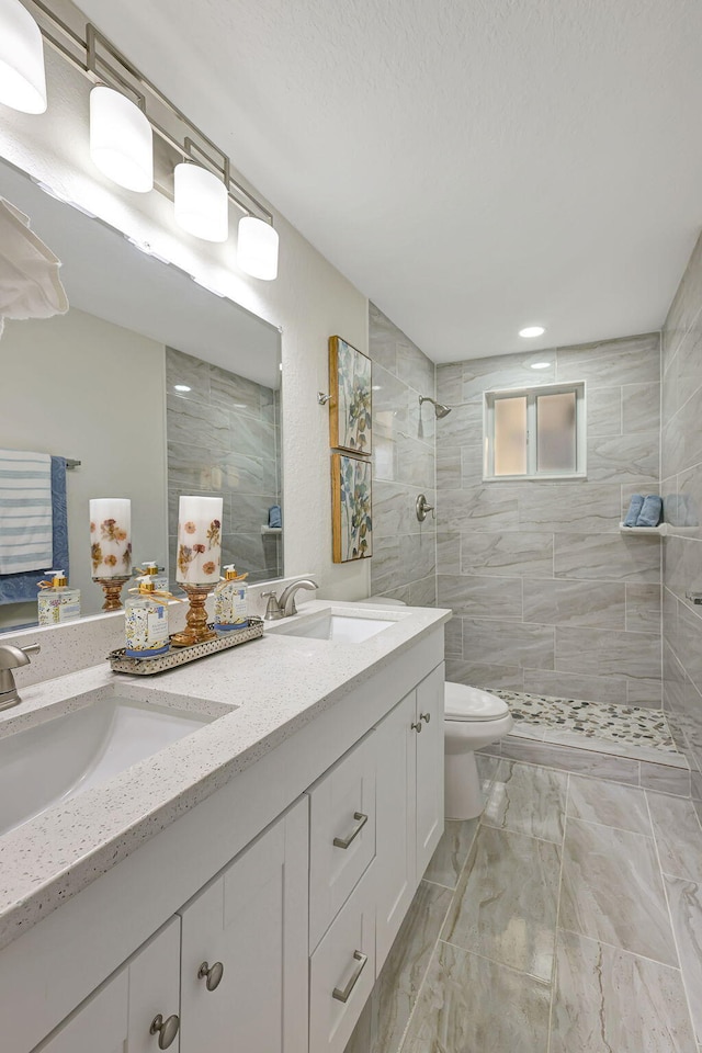 bathroom featuring a tile shower, vanity, and toilet