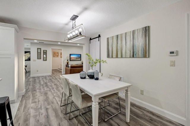 dining area with a barn door, a chandelier, a textured ceiling, and light wood-type flooring