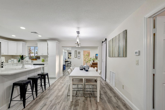 dining room with a textured ceiling, a barn door, light hardwood / wood-style floors, and sink