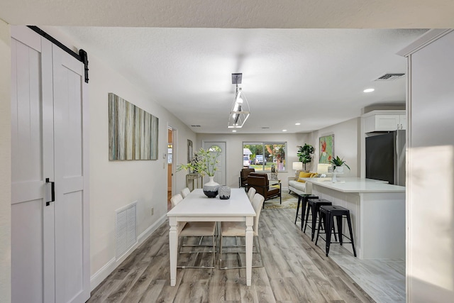 dining room featuring a textured ceiling, a barn door, and light hardwood / wood-style flooring