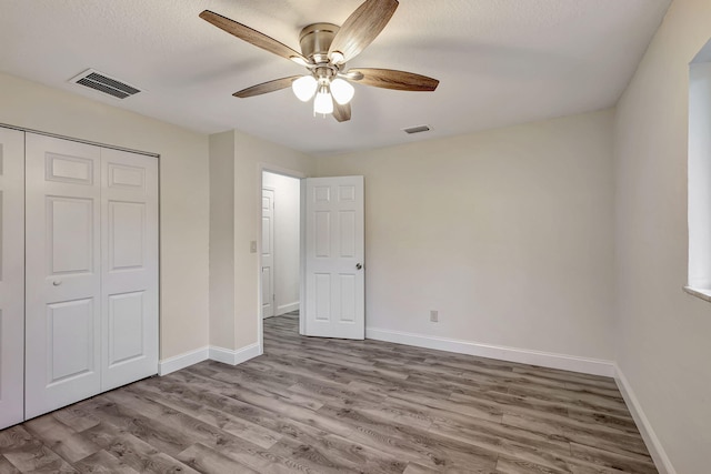 unfurnished bedroom with ceiling fan, light hardwood / wood-style floors, a textured ceiling, and a closet