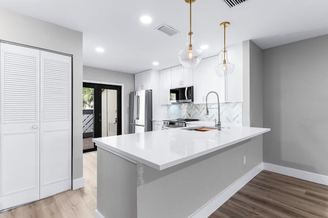 kitchen featuring kitchen peninsula, stainless steel appliances, decorative light fixtures, light hardwood / wood-style flooring, and white cabinets