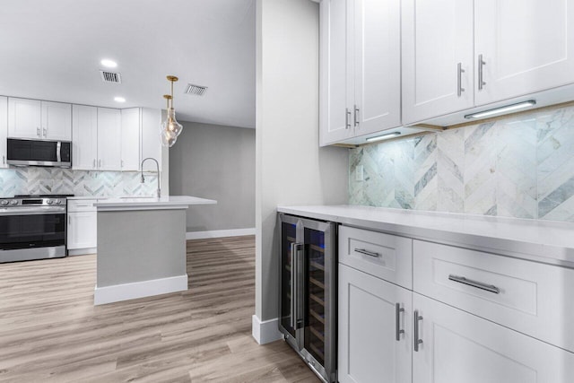 kitchen with pendant lighting, white cabinets, wine cooler, light hardwood / wood-style flooring, and stainless steel appliances