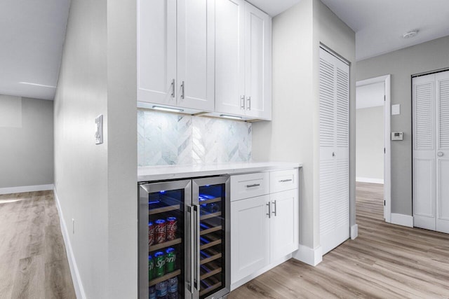 bar featuring tasteful backsplash, white cabinets, beverage cooler, and light wood-type flooring