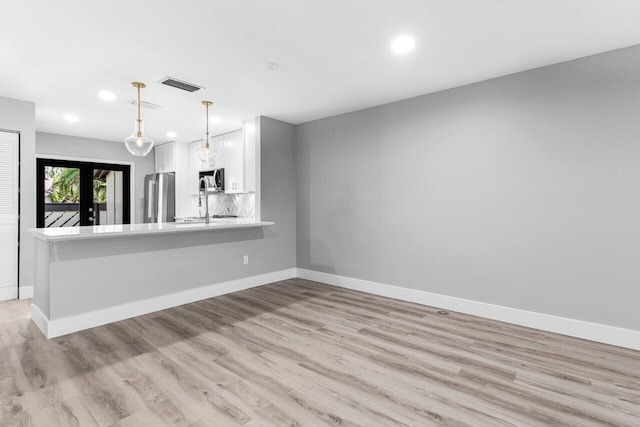 interior space featuring kitchen peninsula, light wood-type flooring, stainless steel appliances, decorative light fixtures, and white cabinets