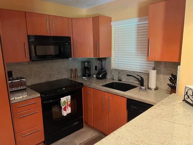 kitchen with sink, tasteful backsplash, light stone counters, light tile patterned floors, and black appliances