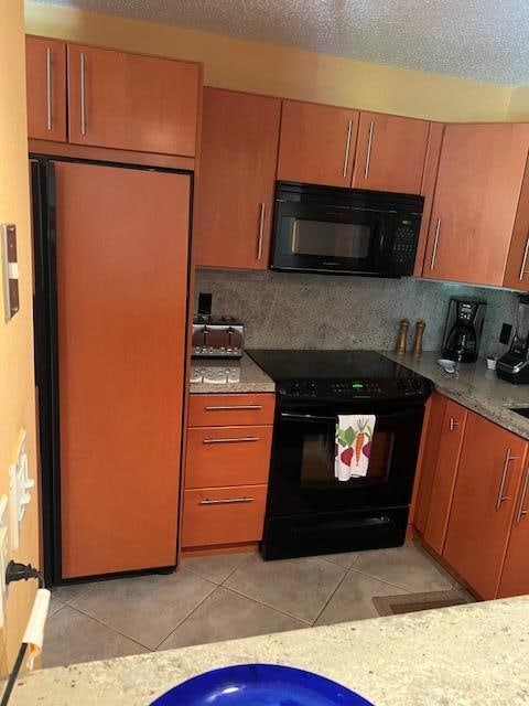 kitchen featuring light tile patterned floors, tasteful backsplash, light stone counters, and black appliances