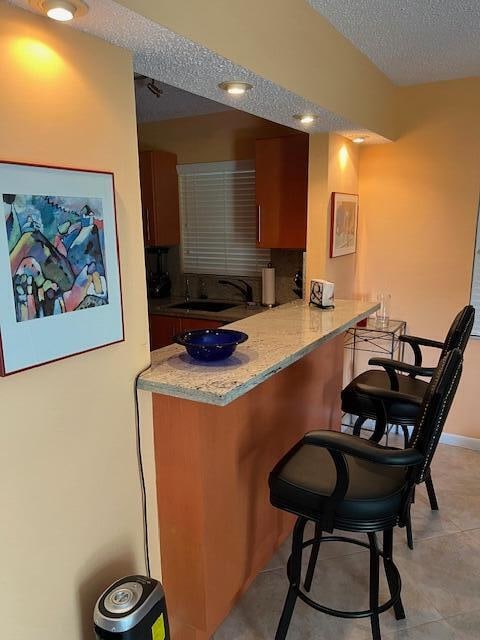 kitchen featuring a kitchen bar, kitchen peninsula, a textured ceiling, sink, and light tile patterned floors