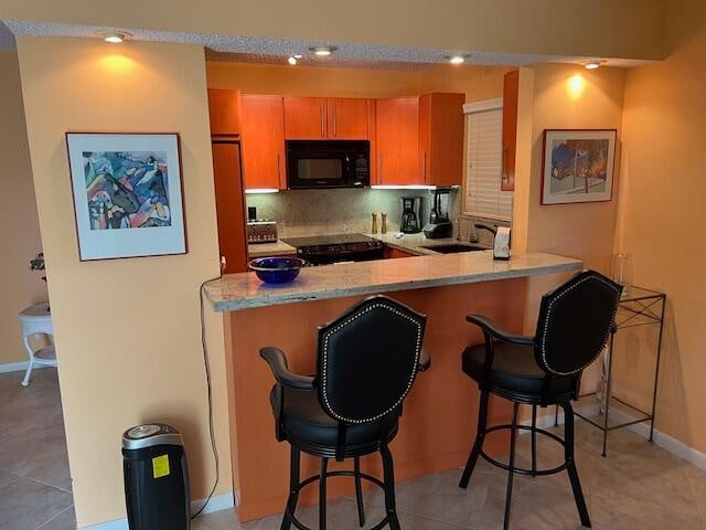 kitchen with light stone countertops, sink, a breakfast bar area, decorative backsplash, and light tile patterned floors