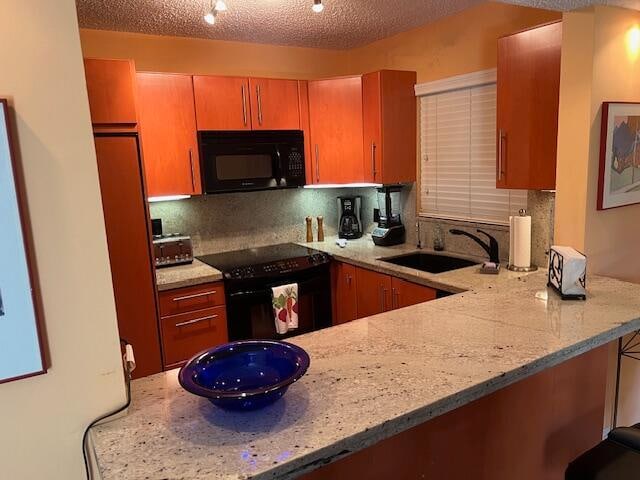 kitchen with kitchen peninsula, backsplash, light stone counters, sink, and black appliances