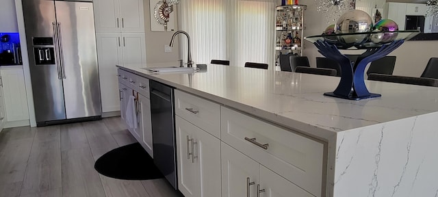 kitchen featuring white cabinetry, sink, light hardwood / wood-style flooring, stainless steel fridge, and a center island with sink