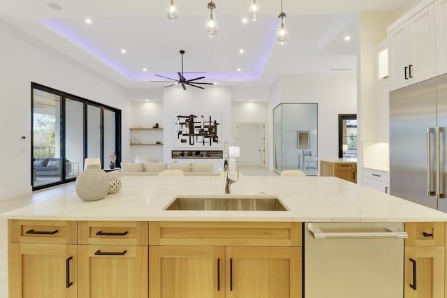 kitchen featuring a large island with sink, sink, light brown cabinets, and a tray ceiling