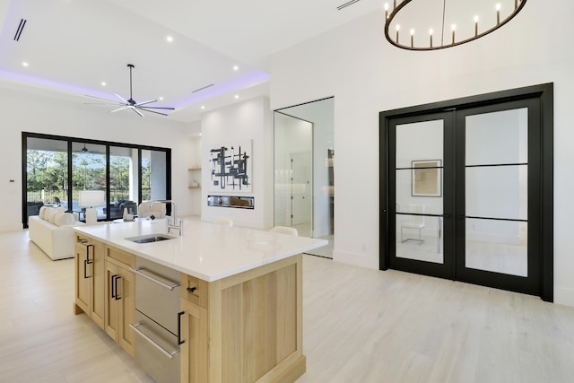 kitchen with sink, light hardwood / wood-style floors, an island with sink, french doors, and light brown cabinets