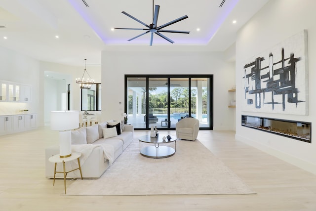 living room with a tray ceiling, ceiling fan with notable chandelier, light hardwood / wood-style floors, and a towering ceiling