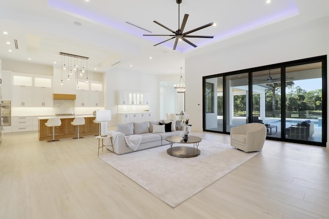 living room with a raised ceiling, ceiling fan, and light wood-type flooring