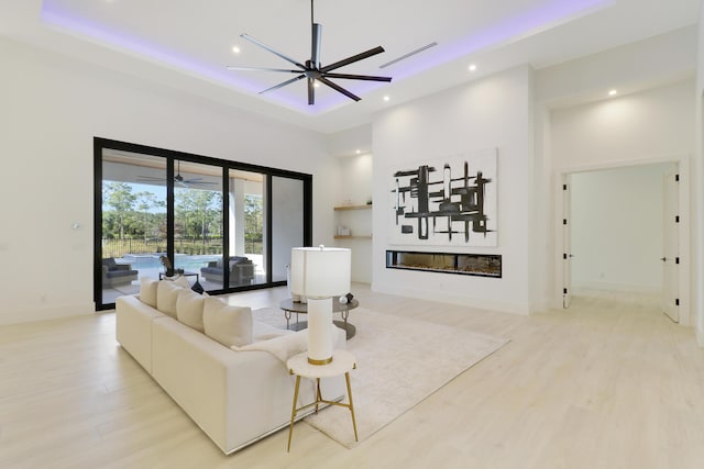 living room with a high ceiling, a raised ceiling, ceiling fan, and light wood-type flooring