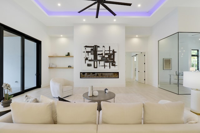 living room featuring ceiling fan, a tray ceiling, a high ceiling, and light wood-type flooring