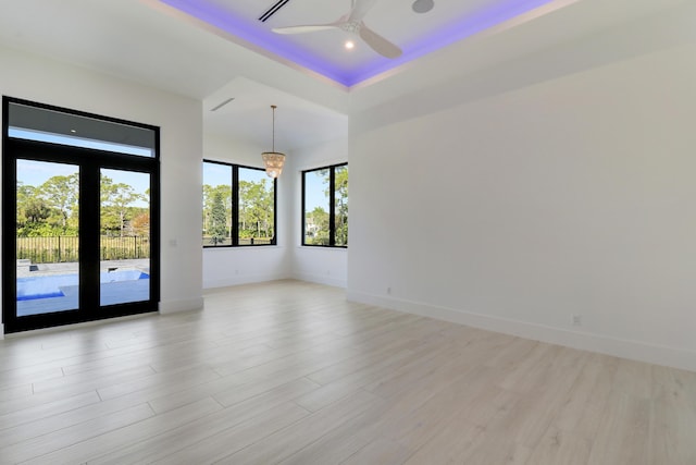 unfurnished room featuring ceiling fan with notable chandelier, light hardwood / wood-style flooring, and a tray ceiling