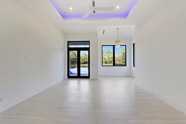 unfurnished room with ceiling fan, light hardwood / wood-style floors, a raised ceiling, and french doors