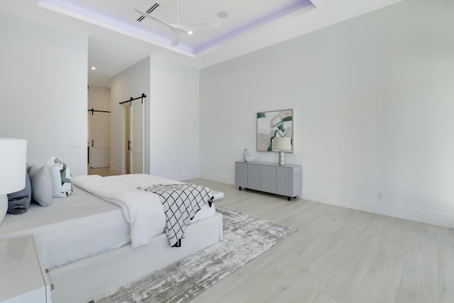 bedroom featuring a raised ceiling, a barn door, radiator heating unit, and light hardwood / wood-style flooring