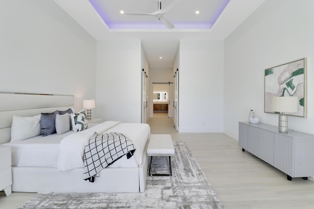 bedroom featuring ensuite bath, light hardwood / wood-style flooring, a barn door, and a high ceiling