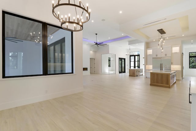 unfurnished living room with ceiling fan with notable chandelier, sink, a tray ceiling, and light hardwood / wood-style floors