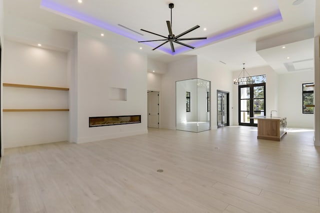 unfurnished living room with a towering ceiling, french doors, ceiling fan, a tray ceiling, and light hardwood / wood-style flooring