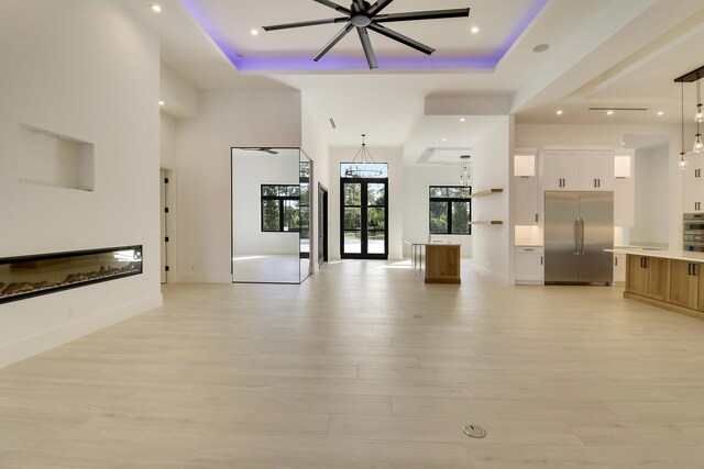 unfurnished living room with light hardwood / wood-style floors, a high ceiling, a tray ceiling, and french doors