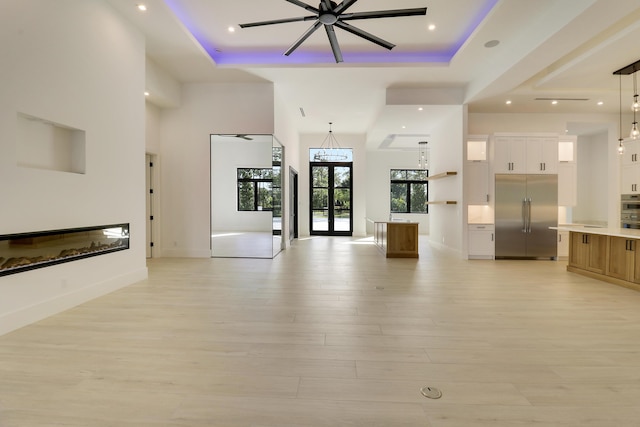 unfurnished living room featuring a tray ceiling, french doors, a high ceiling, and light wood-type flooring