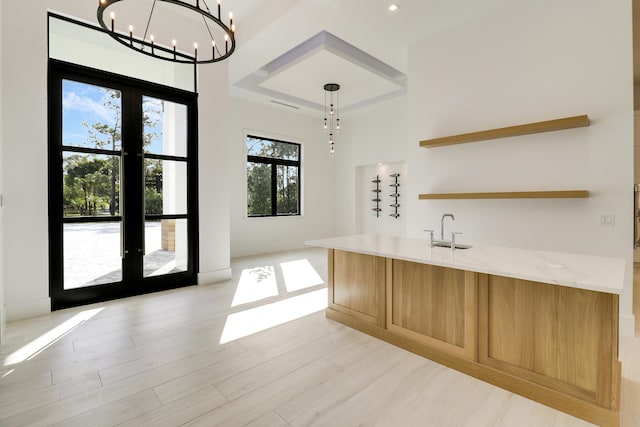 interior space featuring decorative light fixtures, sink, light hardwood / wood-style flooring, french doors, and light stone counters