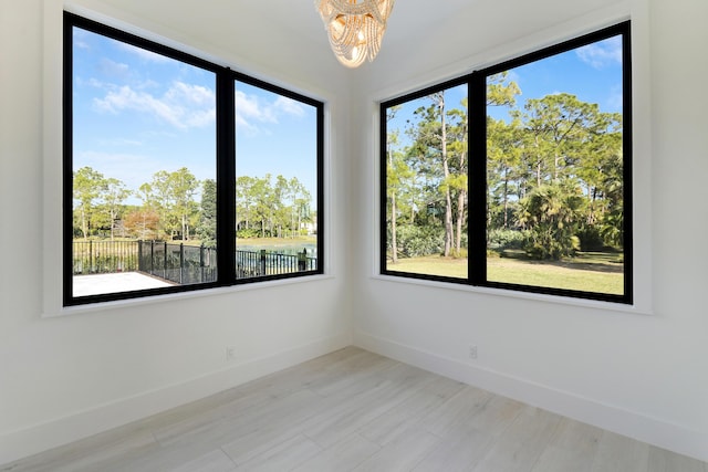 empty room with a water view, an inviting chandelier, and light hardwood / wood-style flooring