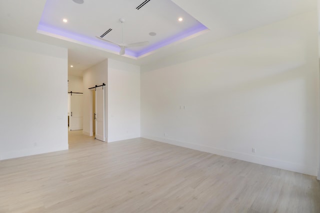 empty room featuring a barn door, a tray ceiling, and light hardwood / wood-style floors