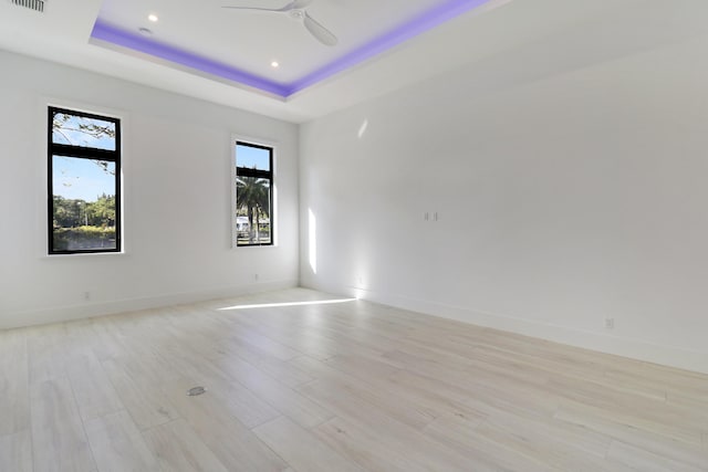 unfurnished room featuring light hardwood / wood-style floors, a tray ceiling, and ceiling fan