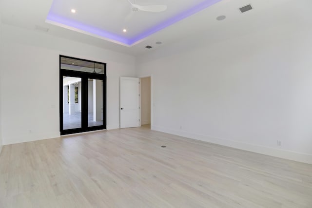 unfurnished room with light wood-type flooring, ceiling fan, a raised ceiling, and french doors