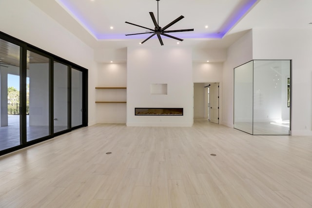 unfurnished living room featuring ceiling fan, light hardwood / wood-style floors, and a tray ceiling