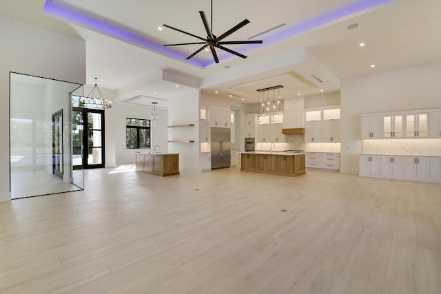 unfurnished living room featuring light wood-type flooring, a towering ceiling, ceiling fan with notable chandelier, and french doors