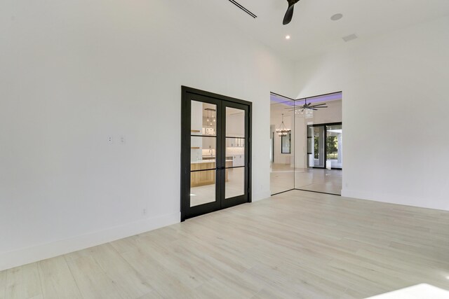 empty room with ceiling fan with notable chandelier, a towering ceiling, light hardwood / wood-style flooring, and french doors