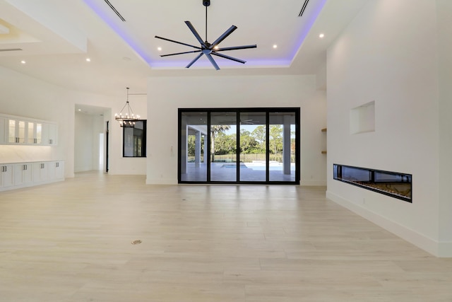 unfurnished living room featuring light wood-type flooring, ceiling fan with notable chandelier, and a raised ceiling