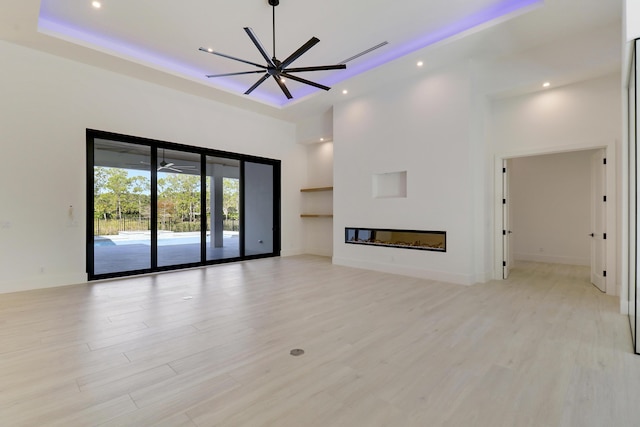 unfurnished living room with ceiling fan, a raised ceiling, and light hardwood / wood-style flooring